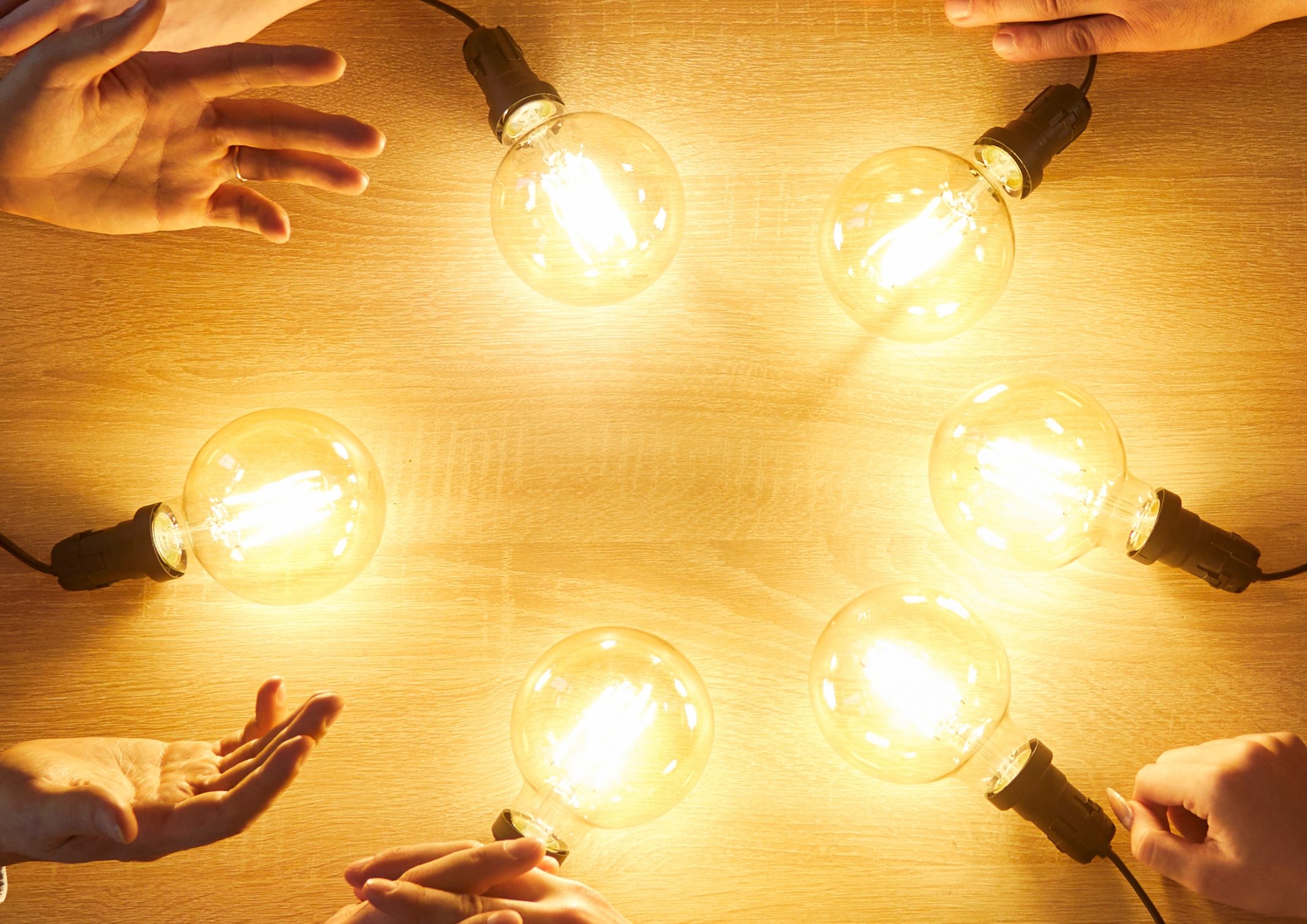 Des mains touchent des ampoules lumineuses disposées en cercle sur une table en bois.